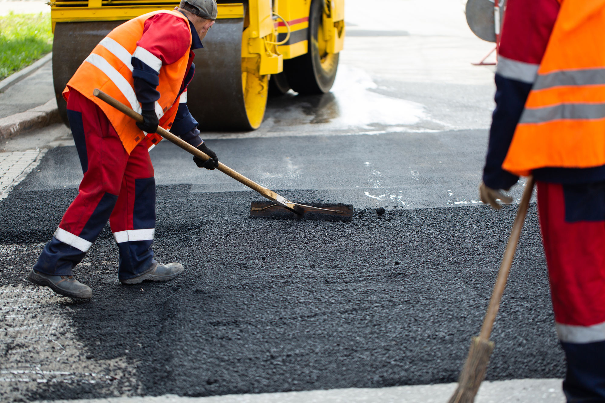 Straßenbauer beim Auftragen von heißem Asphalt und Glätten einer Fahrbahn zur Reparatur